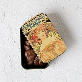 Foto de una lata de hojas de chocolate con leche abierta con las hojas dentro. Real Fábrica.