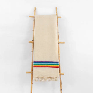 Manta maragata arcoiris crudo expuesta sobre una escalera de madera vintage. La lana es 100% pura de oveja, y con los procesos de fabricación se consigue un tejido ligero y que conserva el calor. Real Fábrica.