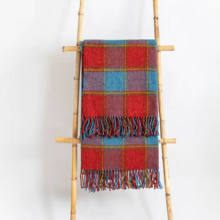 Manta riojana de lana de cuadros en tonos azul y rojo con flecos colgada de una escalera de madera vintage. Real Fábrica