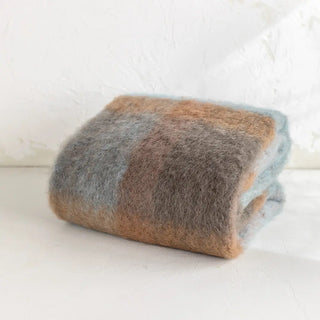 Manta de mohair de cuadros azul y marrón doblada sobre una mesa. En el primer plano se aprecia la textura de la fibra de mohair. Real Fábrica.