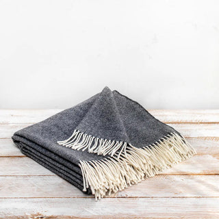 Manta gris oscuro expuesta sobre una mesa de madera elaborada con lana de la sierra de Cádiz, de la que se dice que es de las mejores que te puedes encontrar en España. Real Fábrica