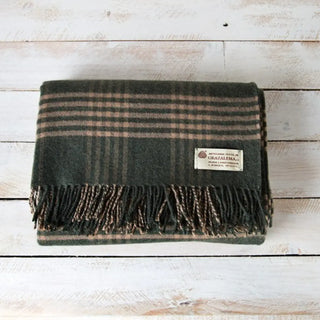 Foto de manda doblada sobre una mesa de madera. Nuestras mantas confeccionadas  a mano en Grazalema, Cádiz. Real Fábrica.