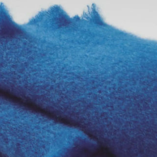 Detalle de manta de mohair en color azul, con terminación en flecos finos. En el primer plano se aprecia la textura de la fibra de mohair. Real Fábrica.