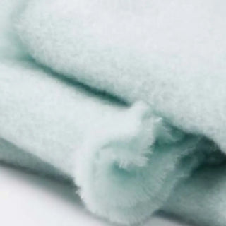 Detalle de manta de mohair en color azul pastel, con terminación en flecos finos. En el primer plano se aprecia la textura de la fibra de mohair. Real Fábrica.