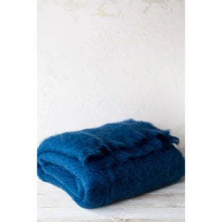 Manta de mohair en color azul, doblada expuesta sobre una mesa de madera. Real Fábrica