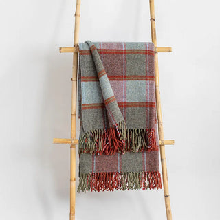 Manta riojana de lana de cuadros en tonos azul celeste con flecos colgada de una escalera de madera vintage. Real Fábrica