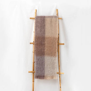 Manta de lana de cuadros en tonos claros tierra con flecos colgada de una escalera vintage. Real Fábrica