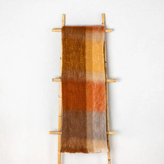 Manta mohair de cuadros marrón, con flecos colgada sobre una escalera de madera vintage. Real Fábrica