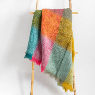 Manta de cuadros expuesta sobre una escalera. Nuestras Mantas mohair de cuadros confeccionada en telares de La Rioja con lana de cabra de angora de la más alta calidad. Real Fábrica.