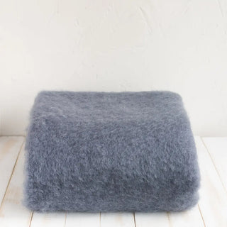 Manta de mohair en color gris azulón doblada sobre una mesa. En el primer plano se aprecia la textura de la fibra de mohair. Real Fábrica.