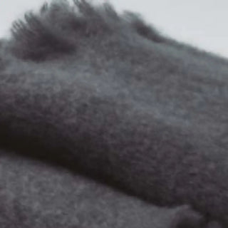 Detalle de manta de mohair gris oscuro, con terminación en flecos finos. En el primer plano se aprecia la textura de la fibra de mohair. Real Fábrica.