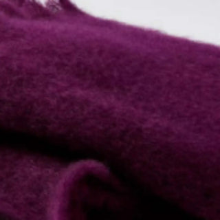 Detalle de manta de mohair en color morado, con terminación en flecos finos. En el primer plano se aprecia la textura de la fibra de mohair. Real Fábrica.