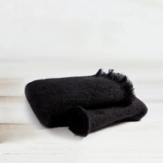 Manta de mohair negra doblada sobre una mesa. En el primer plano se aprecia la textura de la fibra de mohair. Real Fábrica.