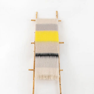 Manta mohair de ezcaray de rayas amarilla flúor negro colgada de una escalera vintage. Real Fábrica.