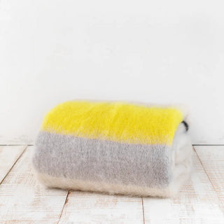Manta de mohair de rayas amarillo flúor negro doblada sobre una mesa. En el primer plano se aprecia la textura de la fibra de mohair. Real Fábrica.