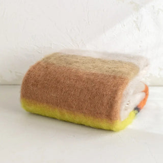 Manta de mohair de rayas amarillo y marrón doblada sobre una mesa. En el primer plano se aprecia la textura de la fibra de mohair. Real Fábrica.