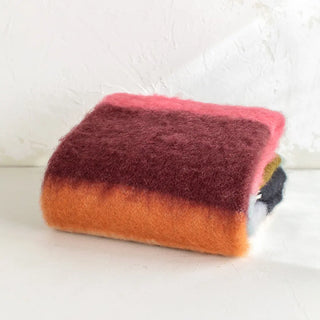 Manta de mohair de rayas negro y buganvilla doblada sobre una mesa. En el primer plano se aprecia la textura de la fibra de mohair. Real Fábrica.