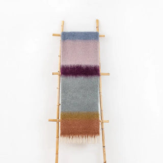 Manta mohair de ezcaray de rayas azul, berenjena y naranja colgada de una escalera vintage. Real Fábrica.