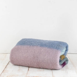 Manta de mohair de rayas azul, berenjena y  naranja doblada sobre una mesa. En el primer plano se aprecia la textura de la fibra de mohair. Real Fábrica.