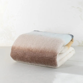 Manta de mohair de rayas marrón, mostaza, marengo doblada sobre una mesa. En el primer plano se aprecia la textura de la fibra de mohair. Real Fábrica.