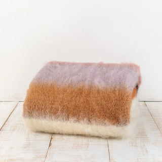 Manta de mohair de rayas rosa, naranja y lila doblada sobre una mesa. En el primer plano se aprecia la textura de la fibra de mohair. Real Fábrica.