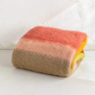 Manta de mohair cuidadosamente doblada. Tiene un diseño de rayas terracota y caldera. Real Fábrica.
