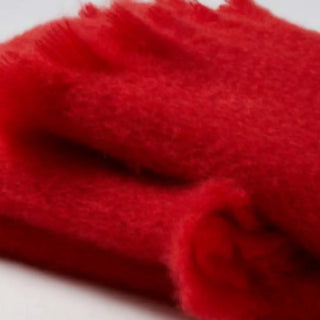 Detalle de manta de mohair en color rojo amapola, con terminación en flecos finos. En el primer plano se aprecia la textura de la fibra de mohair. Real Fábrica.