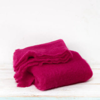 Manta de mohair en color rosa fucsia doblada sobre una mesa. En el primer plano se aprecia la textura de la fibra de mohair. Real Fábrica.