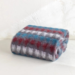 La manta riojana, elaborada a mano con una mezcla de mohair y lana, destaca por su intrincado diseño de círculos, lo que demuestra un trabajo minucioso en cada detalle y una textura suave que proporciona calidez sin exceso de peso. Real Fábrica.