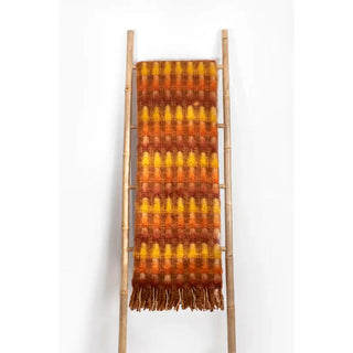 Manta mohair trama mostaza y naranja colgada de escalera de madera. Real Fábrica.