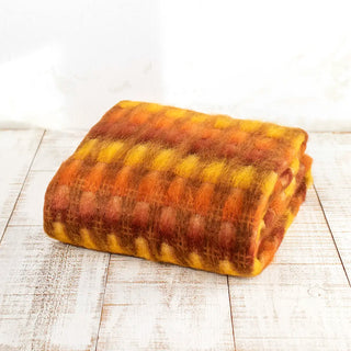Manta mohair trama mostaza y naranja expuesta en forma doblada sobre una mesa de madera. Real Fábrica.