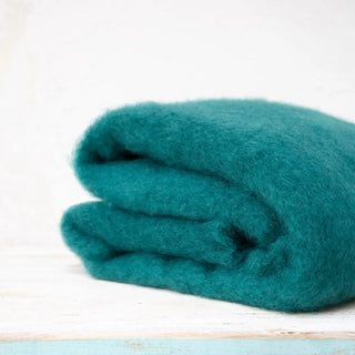 Manta de mohair verde esmeralda doblada sobre una mesa. En el primer plano se aprecia la textura de la fibra de mohair. Real Fábrica.