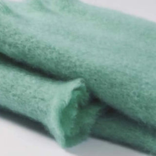 Detalle de manta de mohair en color verde musgo, con terminación en flecos finos. En el primer plano se aprecia la textura de la fibra de mohair. Real Fábrica.