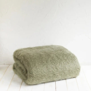 Manta de mohair en color verde oscuro doblada sobre una mesa. En el primer plano se aprecia la textura de la fibra de mohair. Real Fábrica.