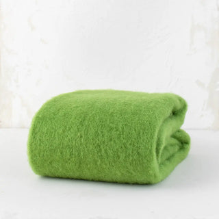 Manta de mohair verde primavera doblada sobre una mesa. En el primer plano se aprecia la textura de la fibra de mohair. Real Fábrica.