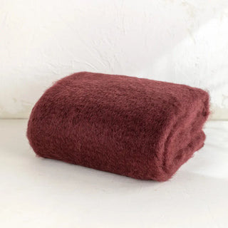 Manta de mohair en color vino tinto doblada sobre una mesa. En el primer plano se aprecia la textura de la fibra de mohair. Real Fábrica.