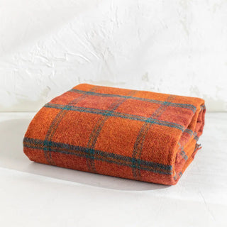 Manta de lana de ezcaray en tonos naranjas y líneas azules expuesta de forma doblada. Real Fábrica