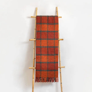 Manta de lana de ezcaray en tonos naranjas y líneas azules colgada de una escalera vintage. Real Fábrica.
