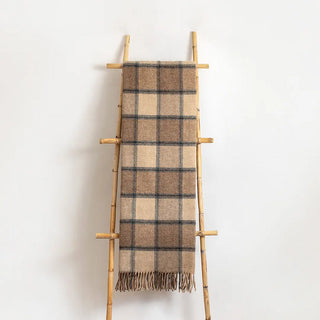 Manta riojana de lana de cuadros en tonos marrones con flecos colgada de una escalera vintage. Real Fábrica