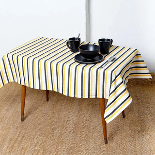 Foto de una mesa vestida con un mantel de tela de algodón con rayas amarilla, negro y blanco, tejido canario loneta algodón con una cerámica negra que lo decora. Real Fábrica.