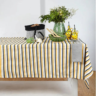 Mantel de rayas amarillas, blancas y negras con vajilla de cerámica verde estilo vegetal y otros accesorios que decoran la mesa, ideal para una mesa fresca y natural. Real Fábrica.