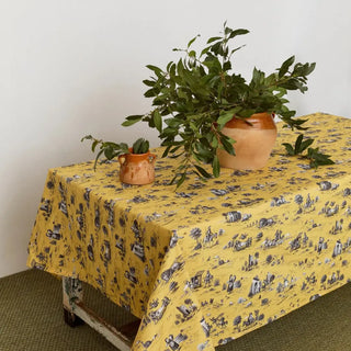 Mantel de la colección Quijote en color amarillo con un centro de mesa marron y hojas verdes. Real Fábrica