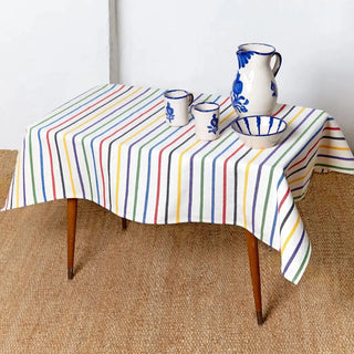Mantel de rayas multicolor con vajilla de cerámica blanca y azul, ideal para una mesa alegre, fresca y con estilo mediterráneo. Real Fábrica.