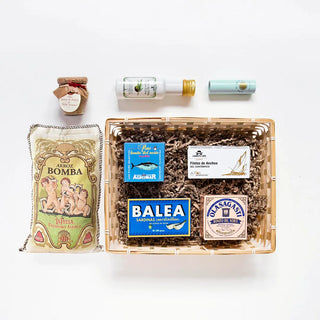 Pack España en Lata de Real Fábrica. Incluye: Paté Bonito del Norte, Bonito del Norte Vasco, Sal de Ibiza mini, Aceite Oliva Ajo, Sardinillas Aceite Oliva Balea, Arroz Albufera, Paté ibérico de Bellota, Anchoas del Cantábrico y Bandeja Grande. Foto vista desde arriba, varios productos dentro de la cesta, varios fuera.