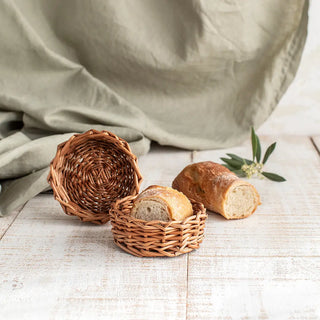 Paneras redondas en mimbre tostado y blanco, perfectas para presentar pan y otros alimentos con estilo. El mimbre decorativo añade un encanto rústico y funcional a la mesa. Real Fábrica.