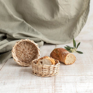 Conjunto de paneras redondas de mimbre en tonos tostado y blanco, útiles para servir pan y decorar mesas. El mimbre ofrece durabilidad y un diseño atractivo para cualquier ocasión. Real Fábrica.