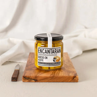 Tarro de cristal de queso de oveja en aceite procedente del pirineo aragonés sobre una tabla de madera y un cuchillo. Real Fábrica.