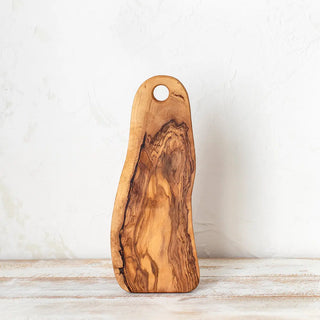 Foto frontal de tabla de madera de olivo en posición vertical sobre una mesa rústica blanca. Real Fábrica.