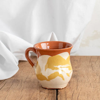 Taza de café abombada de color amarillo y blanco sonre una mesa de madera. Real Fábrica