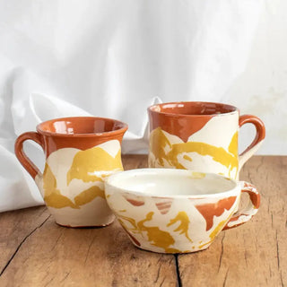 Taza de café de cerámica amarilla y blanca junto con otras tazas hechas con la misma técnica. Real Fábrica